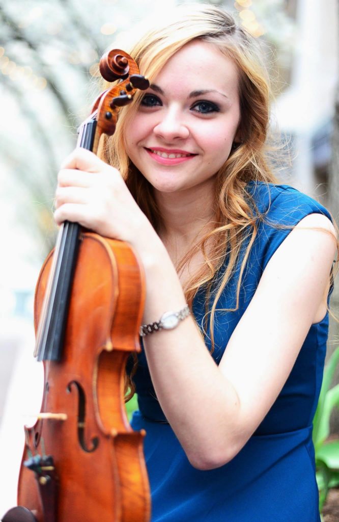 Geigerin Holly Workman holding her violin outside and smiling at the camera for a headshot