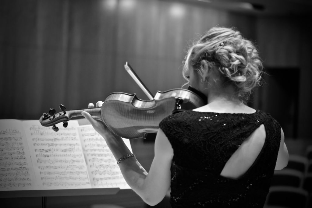 Holly Workman performing in a violin recital. Black and white image taken from behind